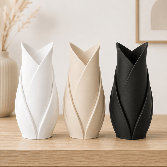 Three modern 3D printed tulip-shaped vases in white, beige, and black, arranged on a light wood surface against a soft neutral background.