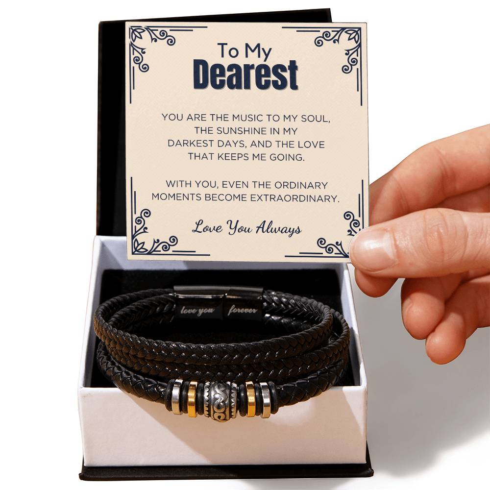 A hand holding a black vegan leather bracelet with engraved text 'To My Dearest' and 'You Are The Music To My Soul' in a presentation box.