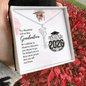Graduation-themed necklace in a gift box with a message and 'Class of 2026' design, held against a red leafy background.