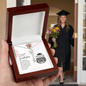 Graduation-themed necklace in a wooden box with a graduate in the background.