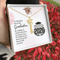 Graduation-themed necklace in a gift box with a message card, surrounded by red foliage.