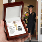 Graduation-themed necklace in a wooden box with a graduate in the background.